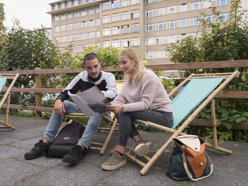 Eine Schülerin und ein Schüler sitzen auf Campingstühlen in der ehemaligen Stasi-Zentrale und blicken in ein Heft aus der Reihe „Quellen für die Schule“