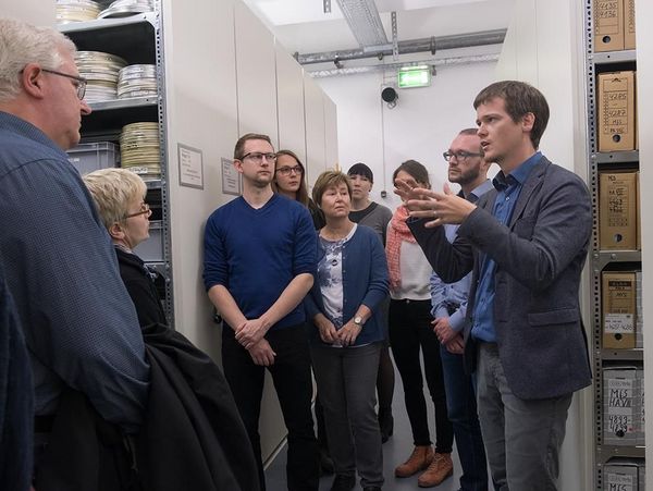 Lehrerinnen und Lehrer stehen vor Archivregalen mit Akten und nehmen an einer Führung teil.